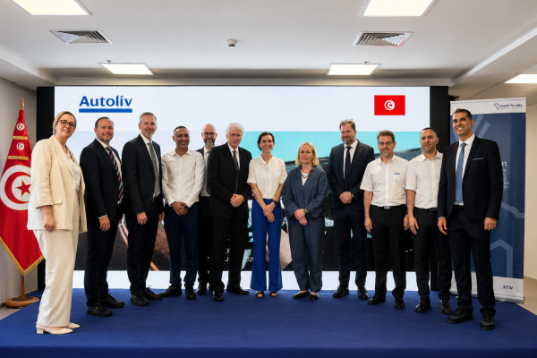 Gruppenfoto von zwölf Gästen in Business-Kleidung auf einer Bühne bei der Eröffnung bei Autoliv Tunisie, vor einem Bildschirm mit dem Autoliv-Logo und der tunesischen Flagge.