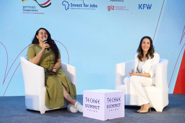 Two women talk in white armchairs on stage at the Techne Summit Cairo, with the Invest for Jobs, GIZ and KfW logos behind them.