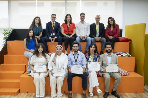 Group photo of twelve people on orange tiered seating; the five in the front row hold up their certificates.