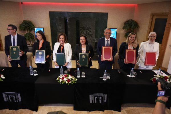 Seven people stand behind a table holding up green and red signing folders after signing an agreement.