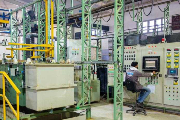 A worker operates an industrial plant from a control panel in a factory hall with green steel frames and tanks.