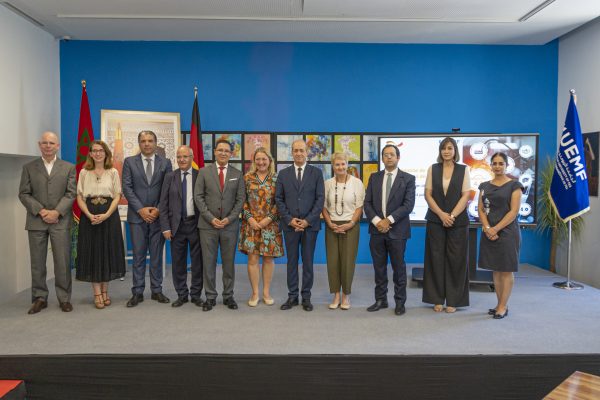 Group photo of twelve people in business attire on a stage in front of a blue wall, with Moroccan, German and UEMF flags.